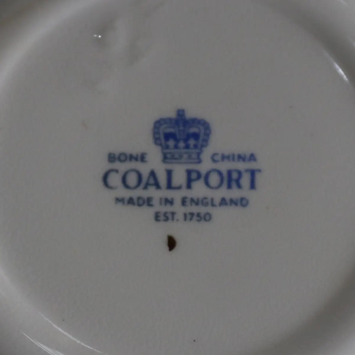 Tazza da tè con piattino in Bone China – Coalport, Inghilterra Raffinata tazza da tè con piattino in fine porcellana Bone China, produzione inglese Coalport, come da marchio al verso con corona e dicitura “Bone China – Coalport – Made in England – Est. 1750”. La tazza, dal corpo leggermente bombato su piede ad anello, è munita di ansa sagomata; il piattino presenta bordo mosso con sottile filettatura in oro. La decorazione, vivace e accurata, raffigura un ricco bouquet floreale policromo con rose e fiori campestri nei toni del rosa, rosso, azzurro e viola, disposto al centro del piattino e sul corpo della tazza. Ottimo stato di conservazione, senza sbeccature o restauri evidenti, con lievi segni d’uso compatibili con l’età. Elegante esempio della tradizione ceramica inglese del Novecento, adatto a collezione o a una tavola in stile classico.