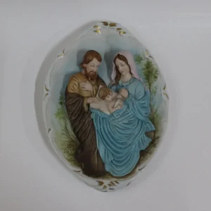 Porcellana di Capodimonte – Madonna con Bambino Ovale da Parete  La Sacra Famiglia in porcellana di Capodimonte è un capolavoro artistico. Quest’opera ovale da parete viene comunemente chiamata Capezzale, questo tipo di opera sono ricercate dai vari collezionisti di arte sacra e non. Il bassorilievo rappresenta una scena piena di dolcezza e armonia. Il tutto è stato curato nei minimi dettagli. I volti sono stati delicatamente dipinti. I colori decisi e sfumati, con predominanza di azzurro, turchese e rosa. L’ovale è finemente decorato lateralmente con eleganti rifiniture in oro, che rende questa porcellana un’opera d’arte di pregio. La combinazione di dettagli raffinati e l’abilità manuale degli artigiani fanno di questa creazione una rappresentazione perfetta della porcellana di Capodimonte, che da sempre è sinonimo di alta qualità artistica e artigianale. Condizioni perfette