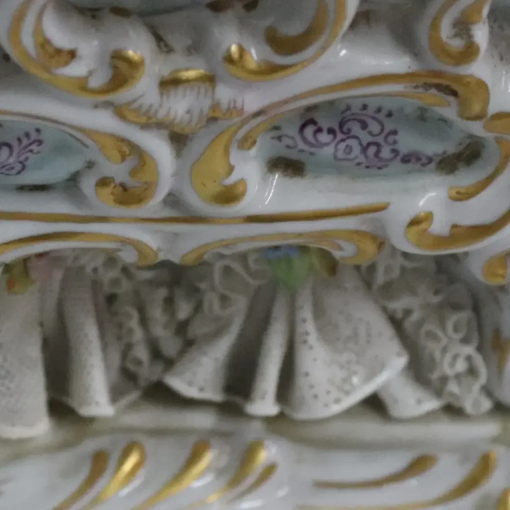 Scultura in porcellana policroma finemente modellata, raffigurante dama in abiti settecenteschi seduta su elegante seduta rocaille. La figura, di gusto rococò, è impreziosita da ricchi decori floreali applicati, delicati motivi dipinti e abbondanti dorature, con accurata resa dei merletti, dei panneggi e dell’acconciatura. La base sagomata, mossa e dorata, completa armoniosamente la composizione. Produzione Capodimonte, Italia, XX secolo, come da marchio al verso; oggetto decorativo di pregio, in buono stato di conservazione.