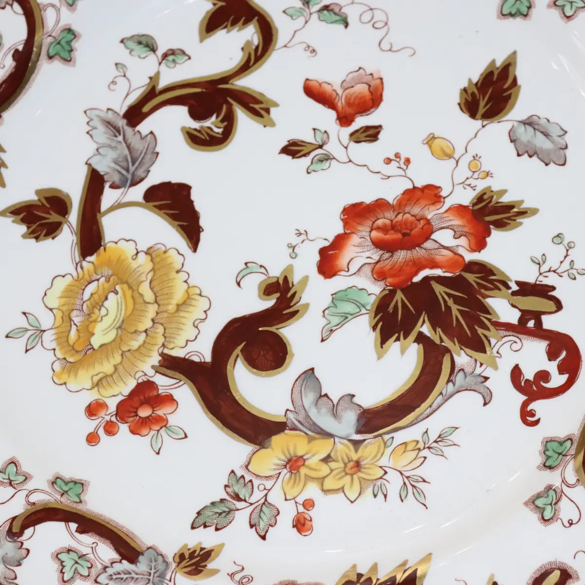 Piatto in ironstone inglese Mason’s, decoro “Velvet Brawn”, con ricche volute brune e fiori policromi in tonalità rosso, giallo e verde su fondo avorio, bordo profilato in oro. Manifattura Staffordshire, prima metà del XX secolo. In buono stato di conservazione.