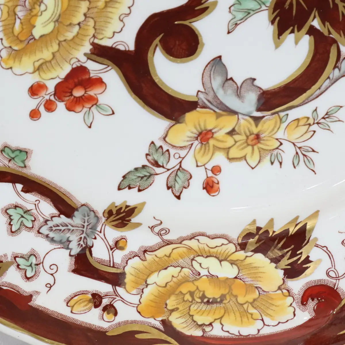 Piatto in ironstone inglese Mason’s, decoro “Velvet Brawn”, con ricche volute brune e fiori policromi in tonalità rosso, giallo e verde su fondo avorio, bordo profilato in oro. Manifattura Staffordshire, prima metà del XX secolo. In buono stato di conservazione.