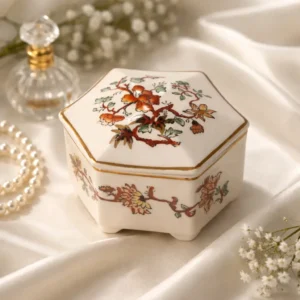 Scatolina esagonale con coperchio in ironstone inglese Mason’s, decorata in policromia con motivo floreale “Golden Azalea” e sottili profili in oro. Fondo color avorio, piedini sagomati e stampa sottosmalto. Marchio al fondo “Mason’s Patent Ironstone – Golden Azalea – Made in England”, databile alla metà del XX secolo. In buono stato di conservazione.