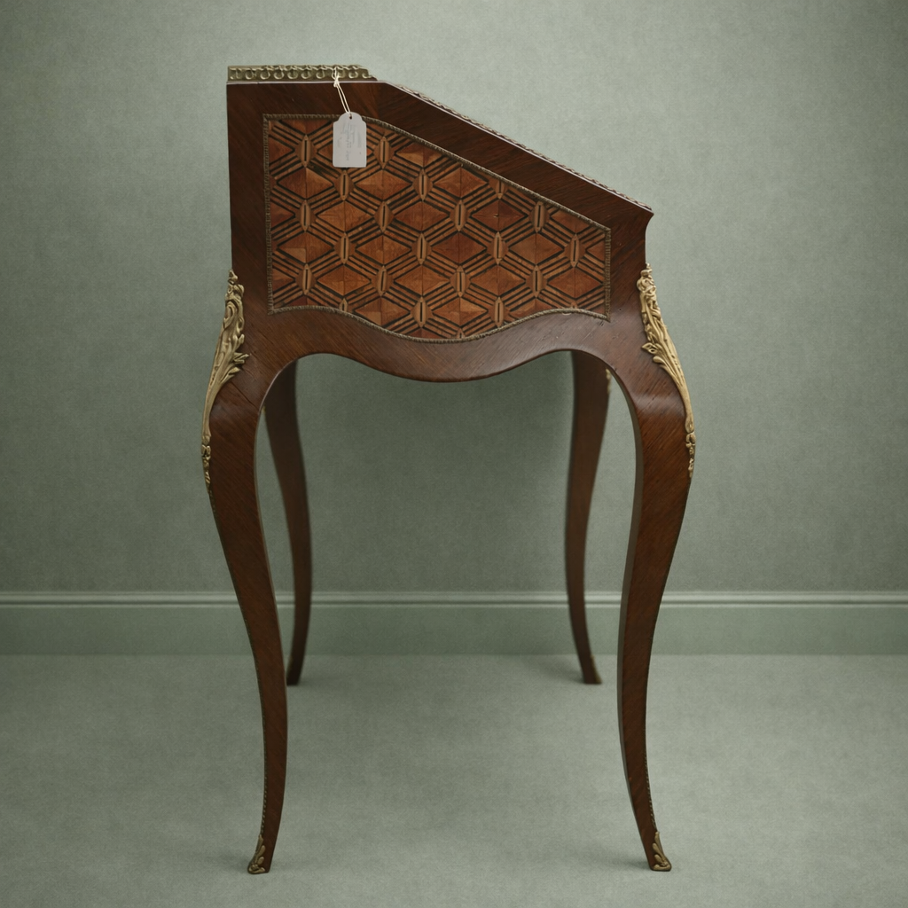 Elegante secrétaire a ribalta in stile Luigi XV, realizzato in legno massello e lastronato con pregiati intarsi geometrici a marqueterie. Il fronte presenta una raffinata ribalta sagomata decorata da motivi romboidali, incorniciata da filettature e arricchita da applicazioni in bronzo dorato. All’interno si trova un piano di scrittura rivestito in panno e una serie di piccoli cassetti impreziositi da marqueterie policrome. Il piano superiore è corredato da una galleria traforata in bronzo, mentre la base poggia su slanciate gambe mosse terminate con calzature in bronzo. Mobile di manifattura di qualità, del XIX secolo, in ottimo stato di conservazione, ideale per ambienti classici ed eleganti.