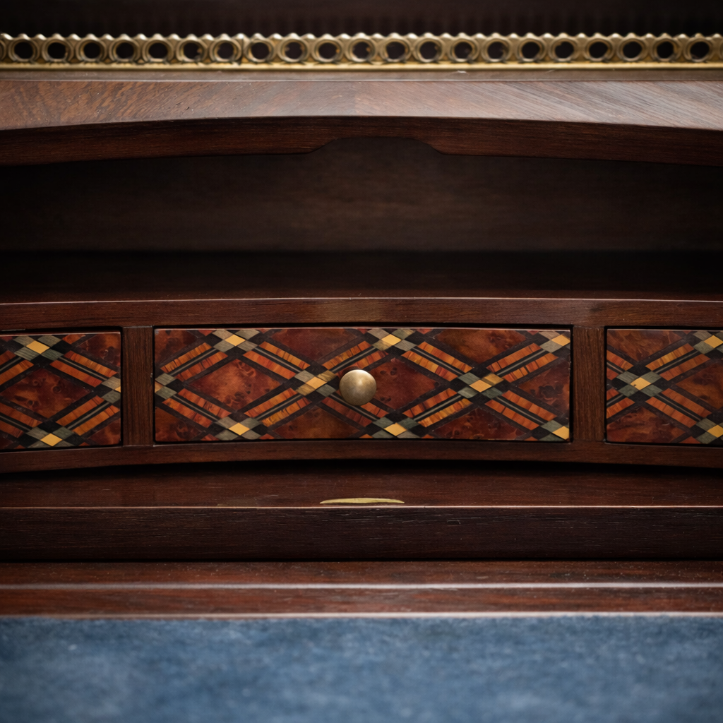 Elegante secrétaire a ribalta in stile Luigi XV, realizzato in legno massello e lastronato con pregiati intarsi geometrici a marqueterie. Il fronte presenta una raffinata ribalta sagomata decorata da motivi romboidali, incorniciata da filettature e arricchita da applicazioni in bronzo dorato. All’interno si trova un piano di scrittura rivestito in panno e una serie di piccoli cassetti impreziositi da marqueterie policrome. Il piano superiore è corredato da una galleria traforata in bronzo, mentre la base poggia su slanciate gambe mosse terminate con calzature in bronzo. Mobile di manifattura di qualità, del XIX secolo, in ottimo stato di conservazione, ideale per ambienti classici ed eleganti.