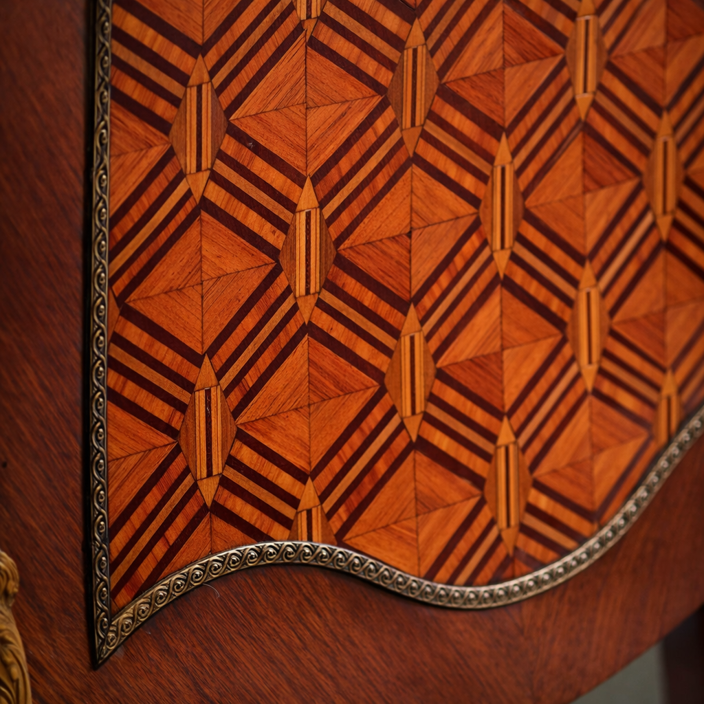 Elegante secrétaire a ribalta in stile Luigi XV, realizzato in legno massello e lastronato con pregiati intarsi geometrici a marqueterie. Il fronte presenta una raffinata ribalta sagomata decorata da motivi romboidali, incorniciata da filettature e arricchita da applicazioni in bronzo dorato. All’interno si trova un piano di scrittura rivestito in panno e una serie di piccoli cassetti impreziositi da marqueterie policrome. Il piano superiore è corredato da una galleria traforata in bronzo, mentre la base poggia su slanciate gambe mosse terminate con calzature in bronzo. Mobile di manifattura di qualità, del XIX secolo, in ottimo stato di conservazione, ideale per ambienti classici ed eleganti.