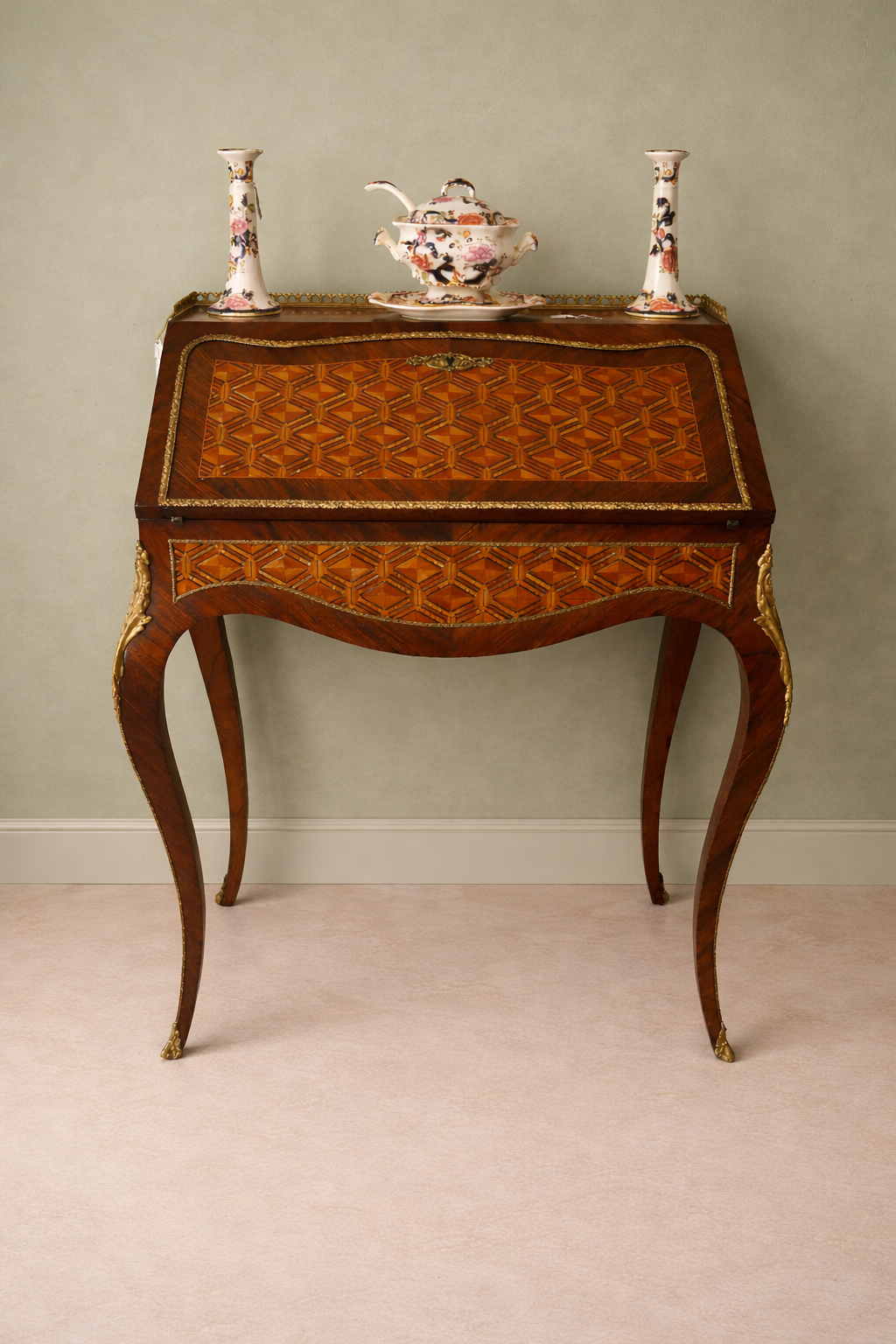 Elegante secrétaire a ribalta in stile Luigi XV, realizzato in legno massello e lastronato con pregiati intarsi geometrici a marqueterie. Il fronte presenta una raffinata ribalta sagomata decorata da motivi romboidali, incorniciata da filettature e arricchita da applicazioni in bronzo dorato. All’interno si trova un piano di scrittura rivestito in panno e una serie di piccoli cassetti impreziositi da marqueterie policrome. Il piano superiore è corredato da una galleria traforata in bronzo, mentre la base poggia su slanciate gambe mosse terminate con calzature in bronzo. Mobile di manifattura di qualità, del XIX secolo, in ottimo stato di conservazione, ideale per ambienti classici ed eleganti.