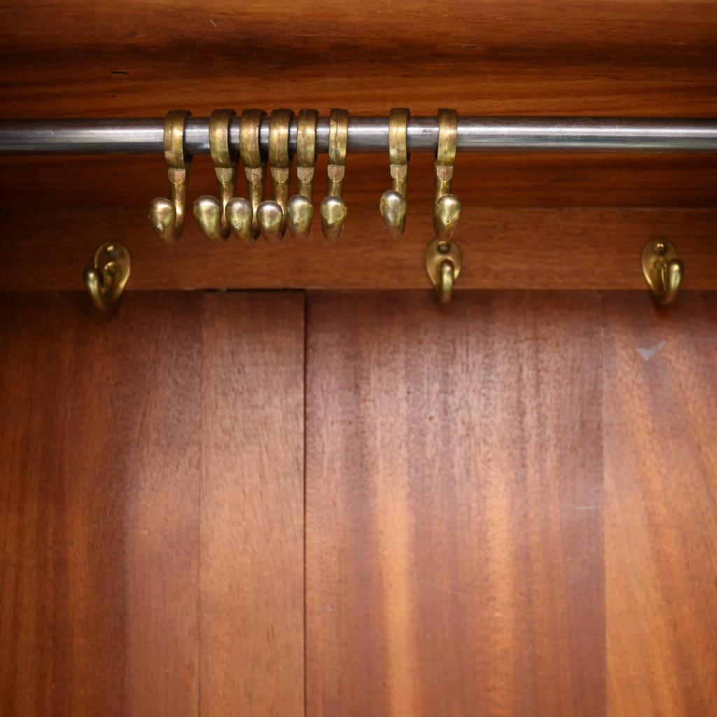 Armadio inglese di gusto Edoardiano, realizzato nei primi anni del XX secolo, in legno di mogano con elegante impiallacciatura a spina di pesce. Struttura architettonica sobria con tre ante, quella centrale a specchio, cappello modanato e cassetto inferiore con pomelli originali in ottone. Interno attrezzato con asta appendiabiti e ganci, finitura calda e ben conservata, tipica della produzione britannica di qualità.