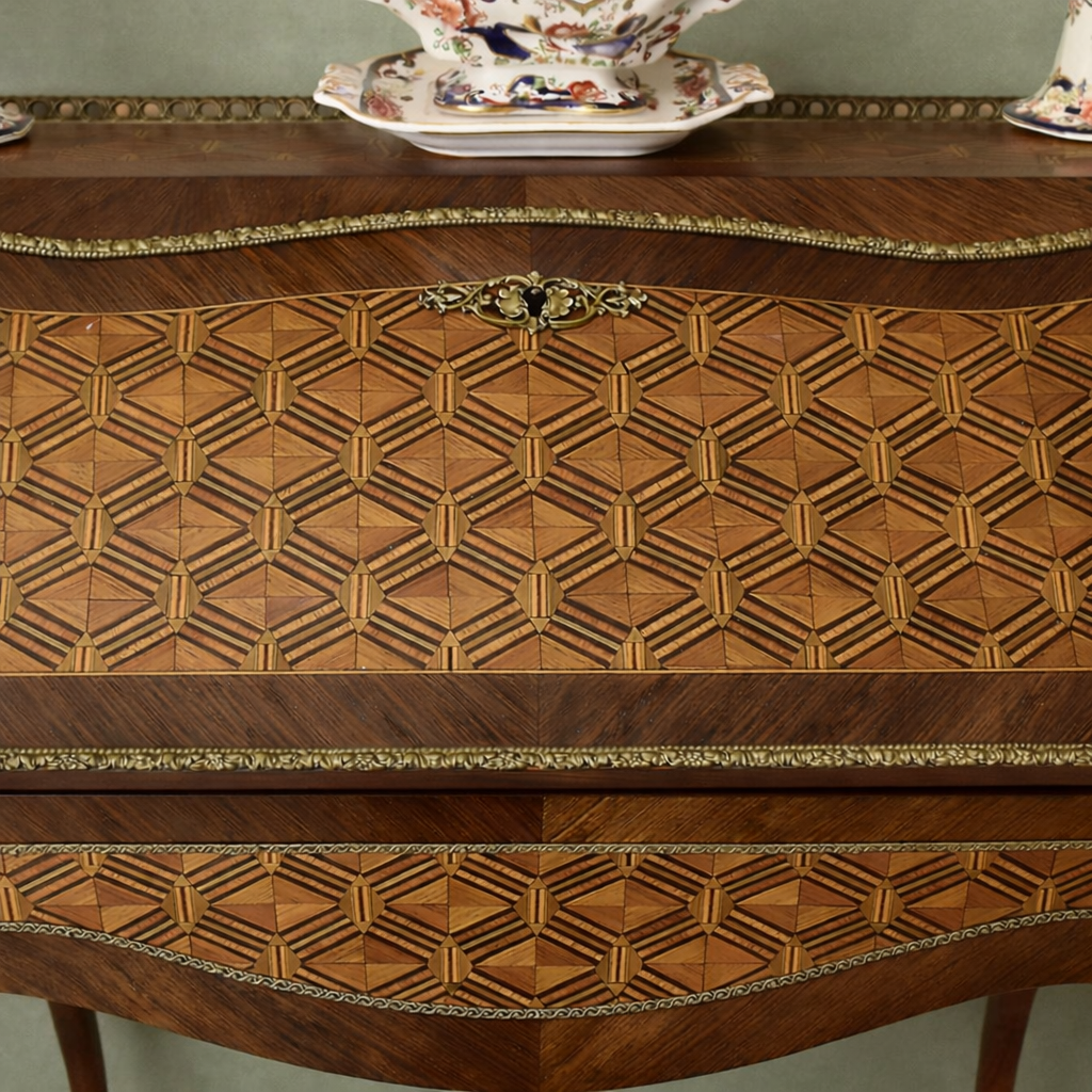 Elegante secrétaire a ribalta in stile Luigi XV, realizzato in legno massello e lastronato con pregiati intarsi geometrici a marqueterie. Il fronte presenta una raffinata ribalta sagomata decorata da motivi romboidali, incorniciata da filettature e arricchita da applicazioni in bronzo dorato. All’interno si trova un piano di scrittura rivestito in panno e una serie di piccoli cassetti impreziositi da marqueterie policrome. Il piano superiore è corredato da una galleria traforata in bronzo, mentre la base poggia su slanciate gambe mosse terminate con calzature in bronzo. Mobile di manifattura di qualità, del XIX secolo, in ottimo stato di conservazione, ideale per ambienti classici ed eleganti.