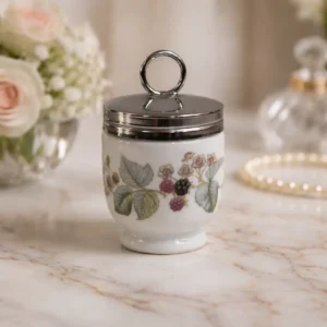 Porta uovo (Egg Coddler) – Royal Worcester, Inghilterra Porta-uovo in porcellana inglese, manifattura Royal Worcester, con corpo cilindrico su piede sagomato e coperchio in metallo argentato con presa ad anello. Decorazione policroma con ramo di more e fogliame, resa con fine naturalismo su fondo bianco. Marchio sul fondo “Royal Worcester – Porcelain – Made in England”. Produzione della prima metà del XX secolo. In buono stato di conservazione.