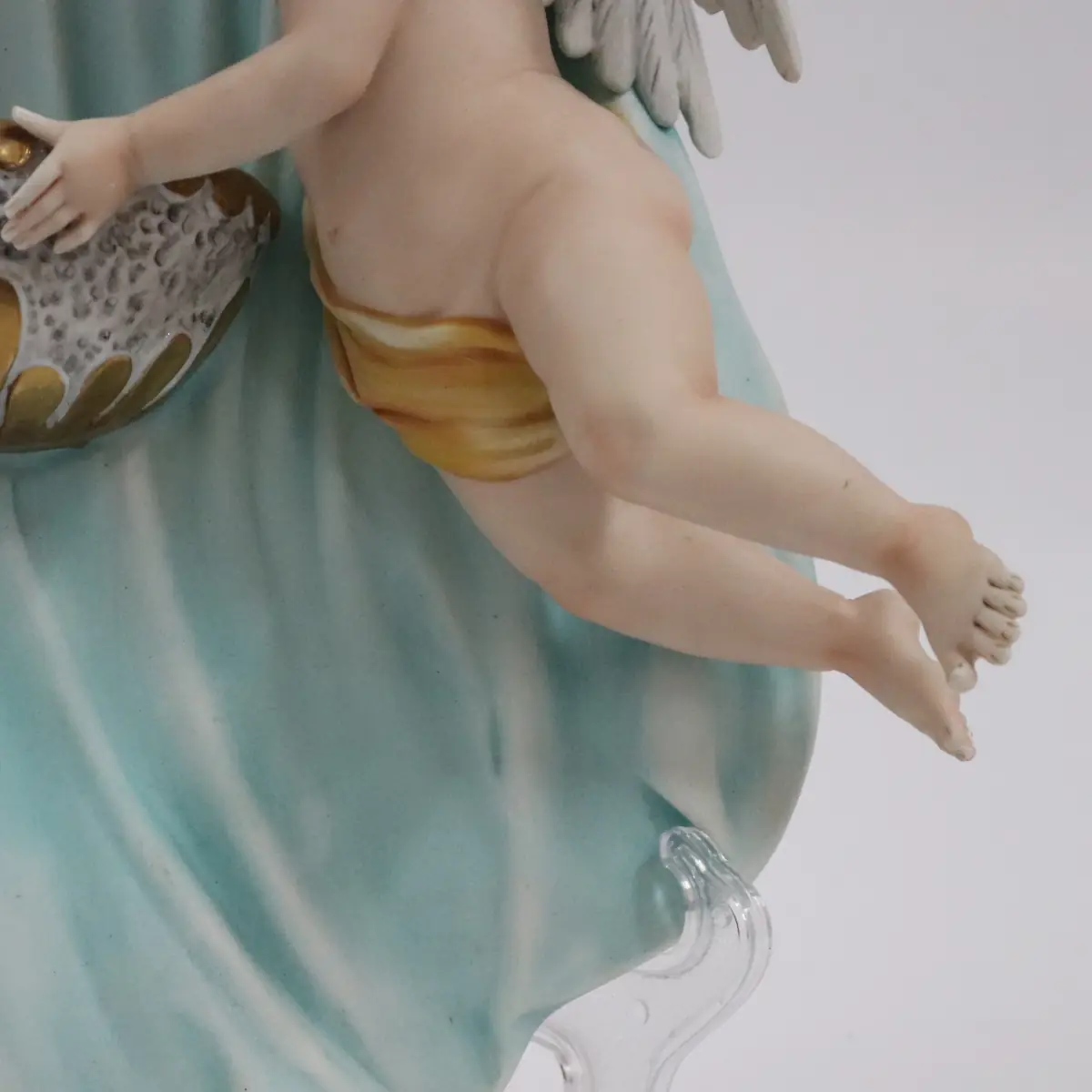Coppia di acquasantiere da parete in porcellana policroma, raffiguranti putti alati modellati a tutto rilievo, sorreggenti vaschette con bordi dorati. Le figure, animate da movimento elegante e panneggi mossi in delicate tonalità pastello, richiamano il gusto tardo barocco–rococò reinterpretato in chiave novecentesca. Produzione italiana, manifattura Corti, XX secolo, destinate all’arredo devozionale domestico; in buono stato di conservazione.