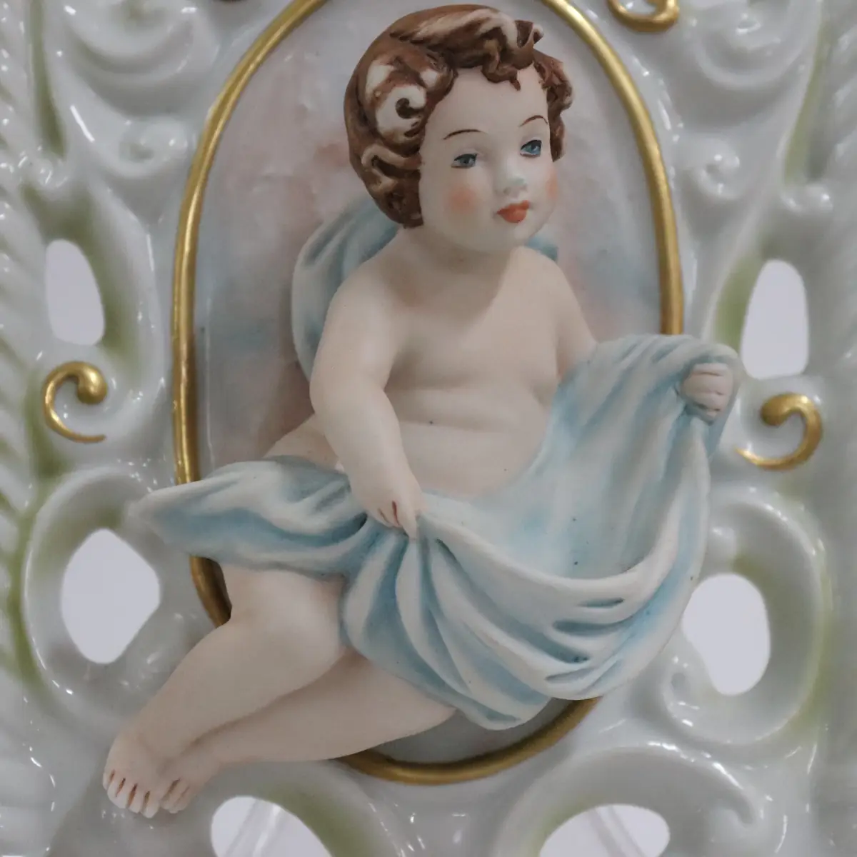Coppia di acquasantiere da parete in porcellana policroma, in stile rococò, con struttura traforata a volute e dorature a rilievo. Al centro, putti modellati a tutto tondo con drappi azzurro e rosato entro riserva ovale. Vaschetta inferiore integrata, decorata con fiori applicati. Produzione italiana Capodimonte, XX secolo, come da marchio con N coronata e firma Corti. In buono stato di conservazione, pregevoli per arredo devozionale e collezione.