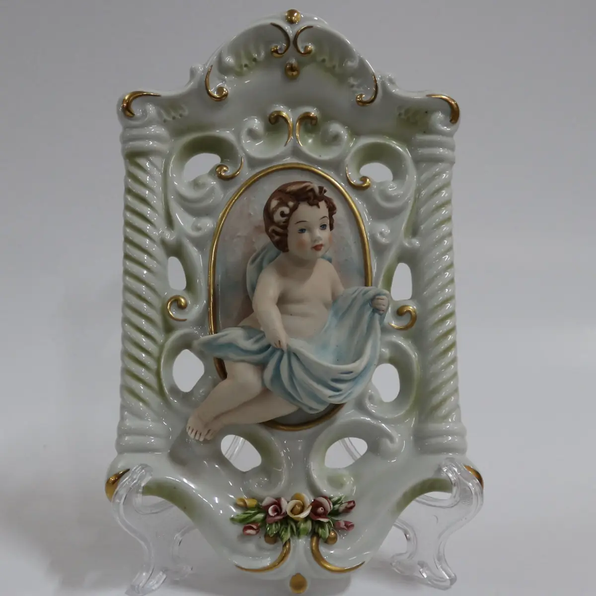 Coppia di acquasantiere da parete in porcellana policroma, in stile rococò, con struttura traforata a volute e dorature a rilievo. Al centro, putti modellati a tutto tondo con drappi azzurro e rosato entro riserva ovale. Vaschetta inferiore integrata, decorata con fiori applicati. Produzione italiana Capodimonte, XX secolo, come da marchio con N coronata e firma Corti. In buono stato di conservazione, pregevoli per arredo devozionale e collezione.