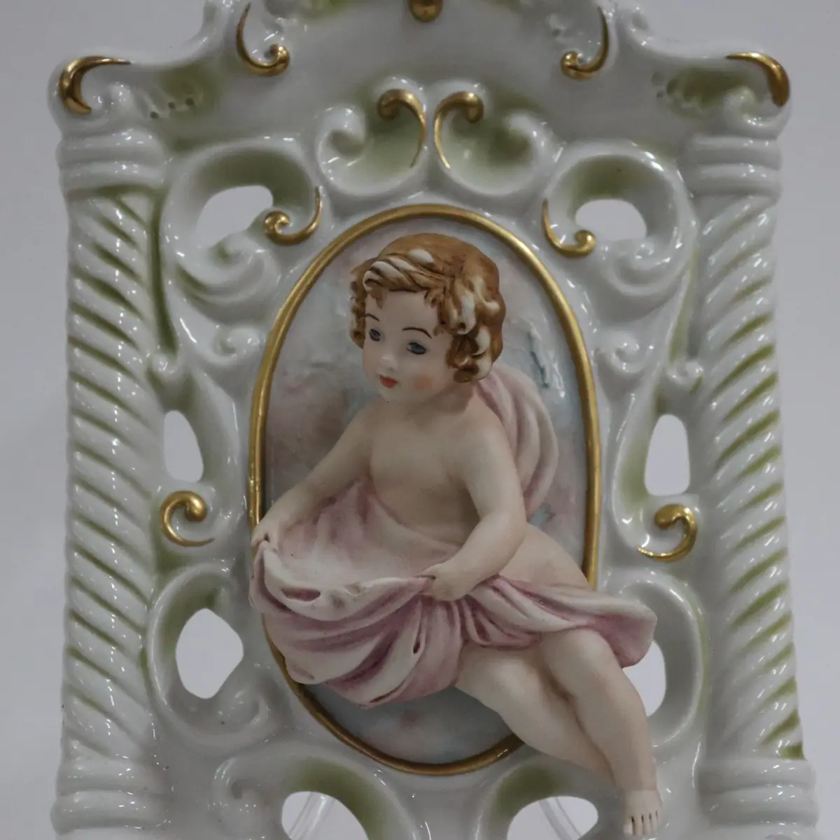 Coppia di acquasantiere da parete in porcellana policroma, in stile rococò, con struttura traforata a volute e dorature a rilievo. Al centro, putti modellati a tutto tondo con drappi azzurro e rosato entro riserva ovale. Vaschetta inferiore integrata, decorata con fiori applicati. Produzione italiana Capodimonte, XX secolo, come da marchio con N coronata e firma Corti. In buono stato di conservazione, pregevoli per arredo devozionale e collezione.
