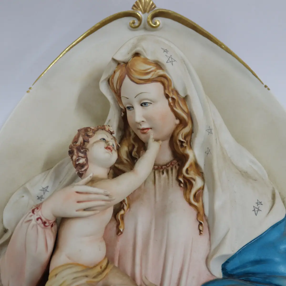 La Madonna con Bambino in porcellana di Capodimonte è un capolavoro artistico, firmato dal Maestro Corti. Quest’opera ovale da parete viene comunemente chiamata Capezzale, creata negli anni ’90 e originariamente distribuita dalla celebre manifattura artigianale King’s, ormai chiusa, è una rarità molto ricercata dai collezionisti di arte sacra. Il bassorilievo rappresenta una scena piena di dolcezza e armonia. La cura nei dettagli si riflette nella perfetta lavorazione delle mani e dei piedi del Bambino, mentre i volti sono stati delicatamente dipinti. I colori decisi e sfumati, con predominanza di azzurro, turchese e rosa. L’ovale è finemente decorato lateralmente con eleganti rifiniture in oro, che rende questa porcellana un’opera d’arte di pregio. La combinazione di dettagli raffinati e l’abilità manuale degli artigiani fanno di questa creazione una rappresentazione perfetta della porcellana di Capodimonte, che da sempre è sinonimo di alta qualità artistica e artigianale. Misure: cm. 47 x 35 x 5 Condizioni perfette
