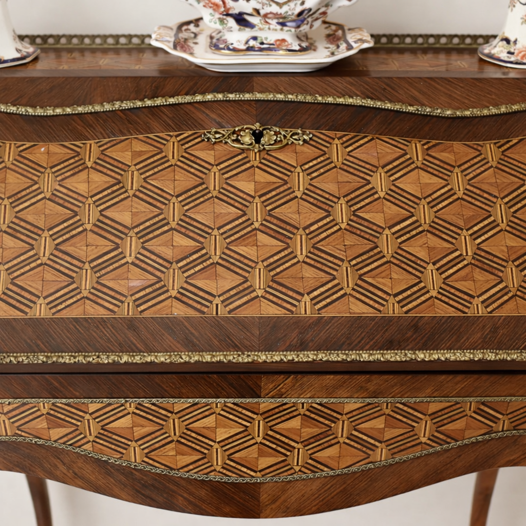 Elegante secrétaire a ribalta in stile Luigi XV, realizzato in legno massello e lastronato con pregiati intarsi geometrici a marqueterie. Il fronte presenta una raffinata ribalta sagomata decorata da motivi romboidali, incorniciata da filettature e arricchita da applicazioni in bronzo dorato. All’interno si trova un piano di scrittura rivestito in panno e una serie di piccoli cassetti impreziositi da marqueterie policrome. Il piano superiore è corredato da una galleria traforata in bronzo, mentre la base poggia su slanciate gambe mosse terminate con calzature in bronzo. Mobile di manifattura di qualità, del XIX secolo, in ottimo stato di conservazione, ideale per ambienti classici ed eleganti.