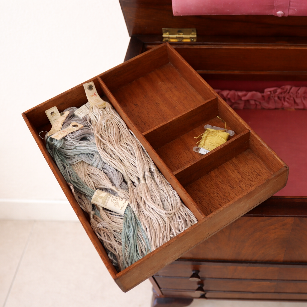 Raffinato sewing cabinet / mobiletto da lavoro inglese dei primi del Novecento, realizzato in legno massello e impiallacciato con bella venatura a specchio sul fronte. Dotato di tre cassetti e piano superiore apribile che nasconde un vano organizzato per il cucito con scomparti interni e rivestimenti in tessuto rosa. Sostenuto da eleganti gambe mosse in stile Queen Anne, presenta linee armoniose e proporzioni equilibrate. Mobile solido, ben conservato, con piacevole patina del tempo. Perfetto come complemento d’arredo o pezzo da collezione.
