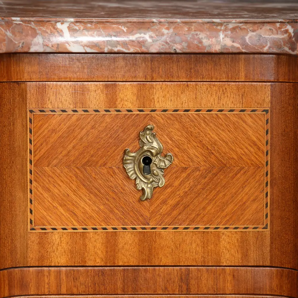 Cassettone bombato francese del XIX secolo con piano in marmo rosso Raffinato cassettone francese dell’Ottocento in stile Luigi XV, caratterizzato da linea mossa e fronte bombato. Realizzato in legni pregiati con impiallacciatura e riserve a intarsio geometrico, presenta tre ampi cassetti impreziositi da maniglie e bocchette in bronzo cesellato, in armonia con le applicazioni angolari e i sabot delle gambe.