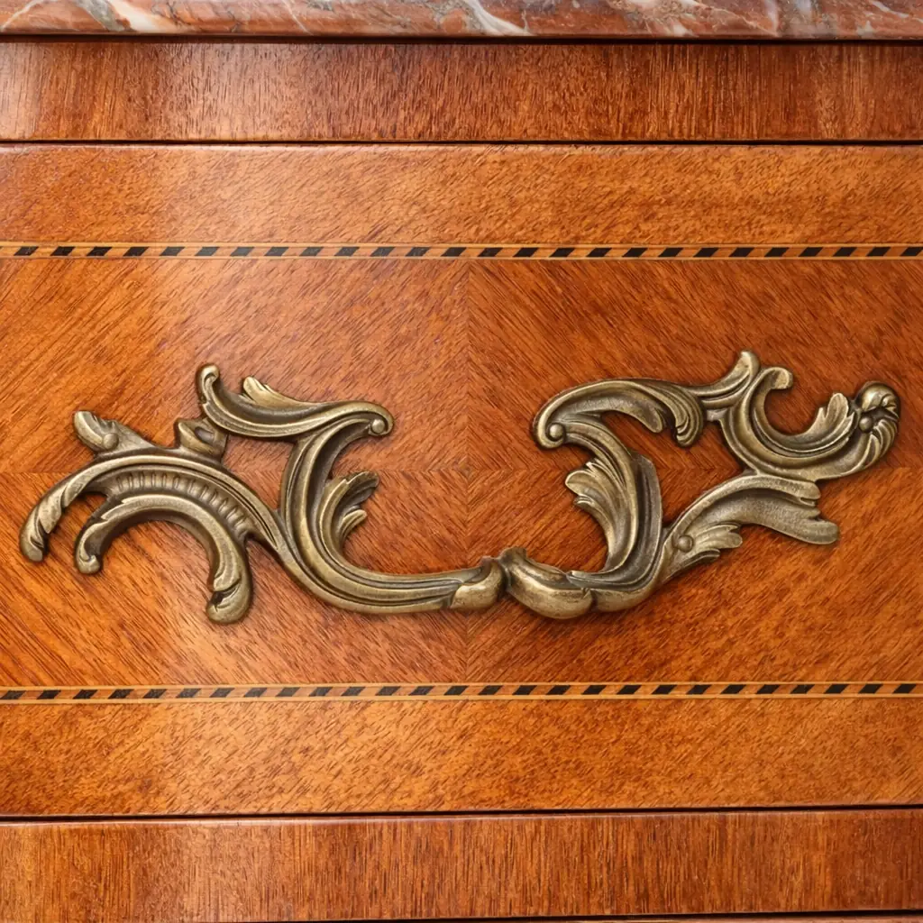 Cassettone bombato francese del XIX secolo con piano in marmo rosso Raffinato cassettone francese dell’Ottocento in stile Luigi XV, caratterizzato da linea mossa e fronte bombato. Realizzato in legni pregiati con impiallacciatura e riserve a intarsio geometrico, presenta tre ampi cassetti impreziositi da maniglie e bocchette in bronzo cesellato, in armonia con le applicazioni angolari e i sabot delle gambe.