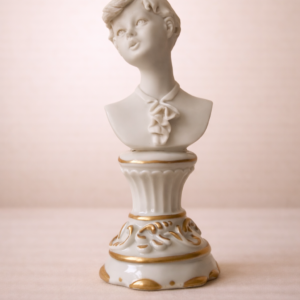 Busto in porcellana di Capodimonte raffigurante giovane fanciullo, XX secolo Busto in porcellana di Capodimonte raffigurante giovane ragazzo, modellato con volto delicato ed espressione assorta, capo leggermente reclinato e acconciatura corta finemente definita. La porcellana, di tonalità avorio, presenta una lavorazione accurata e morbida resa dei volumi. La figura poggia su base sagomata con decorazioni a rilievo e filettature dorate. Manifattura di gusto classicheggiante, destinata al collezionismo e all’arredo di pregio. Stato di conservazione molto buono.