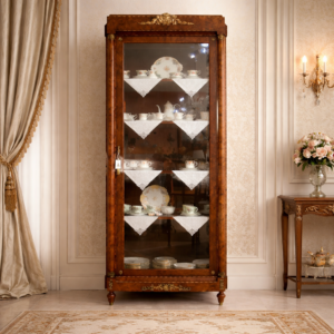 Elegante vetrina a un’anta in legno finemente impiallacciato in radica, con riserve e filettature a contrasto, riconducibile al gusto Luigi XVI / Neoclassico. Struttura architettonica con colonne laterali e anta a vetro originale, arricchita da ricche applicazioni in bronzo dorato: fregio floreale al coronamento, maniglia e guarnizioni finemente cesellate. Interni con ripiani destinati all’esposizione di porcellane. Manifattura francese o mitteleuropea, fine XIX – inizi XX secolo. Buono stato di conservazione, con patina coerente all’età e all’uso.