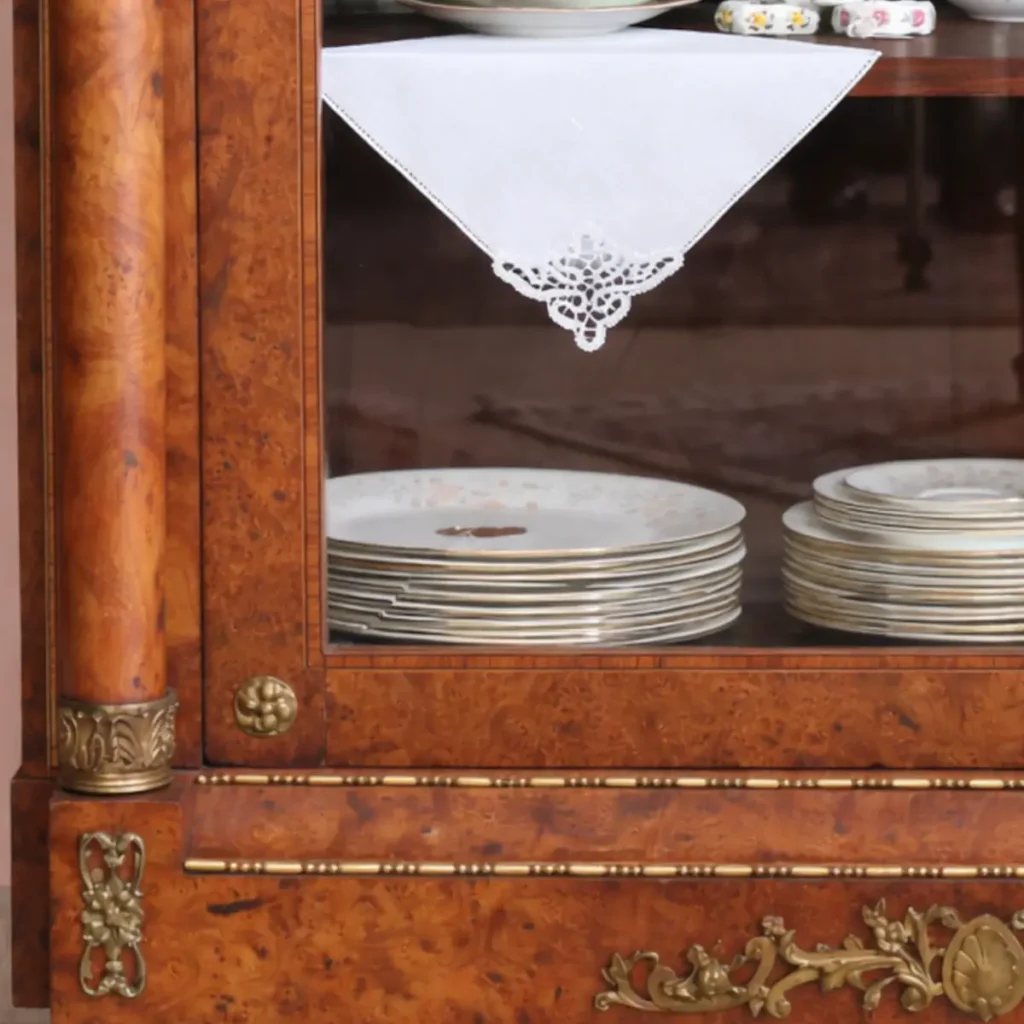 Elegante vetrina a un’anta in legno finemente impiallacciato in radica, con riserve e filettature a contrasto, riconducibile al gusto Luigi XVI / Neoclassico. Struttura architettonica con colonne laterali e anta a vetro originale, arricchita da ricche applicazioni in bronzo dorato: fregio floreale al coronamento, maniglia e guarnizioni finemente cesellate. Interni con ripiani destinati all’esposizione di porcellane. Manifattura francese o mitteleuropea, fine XIX – inizi XX secolo. Buono stato di conservazione, con patina coerente all’età e all’uso.