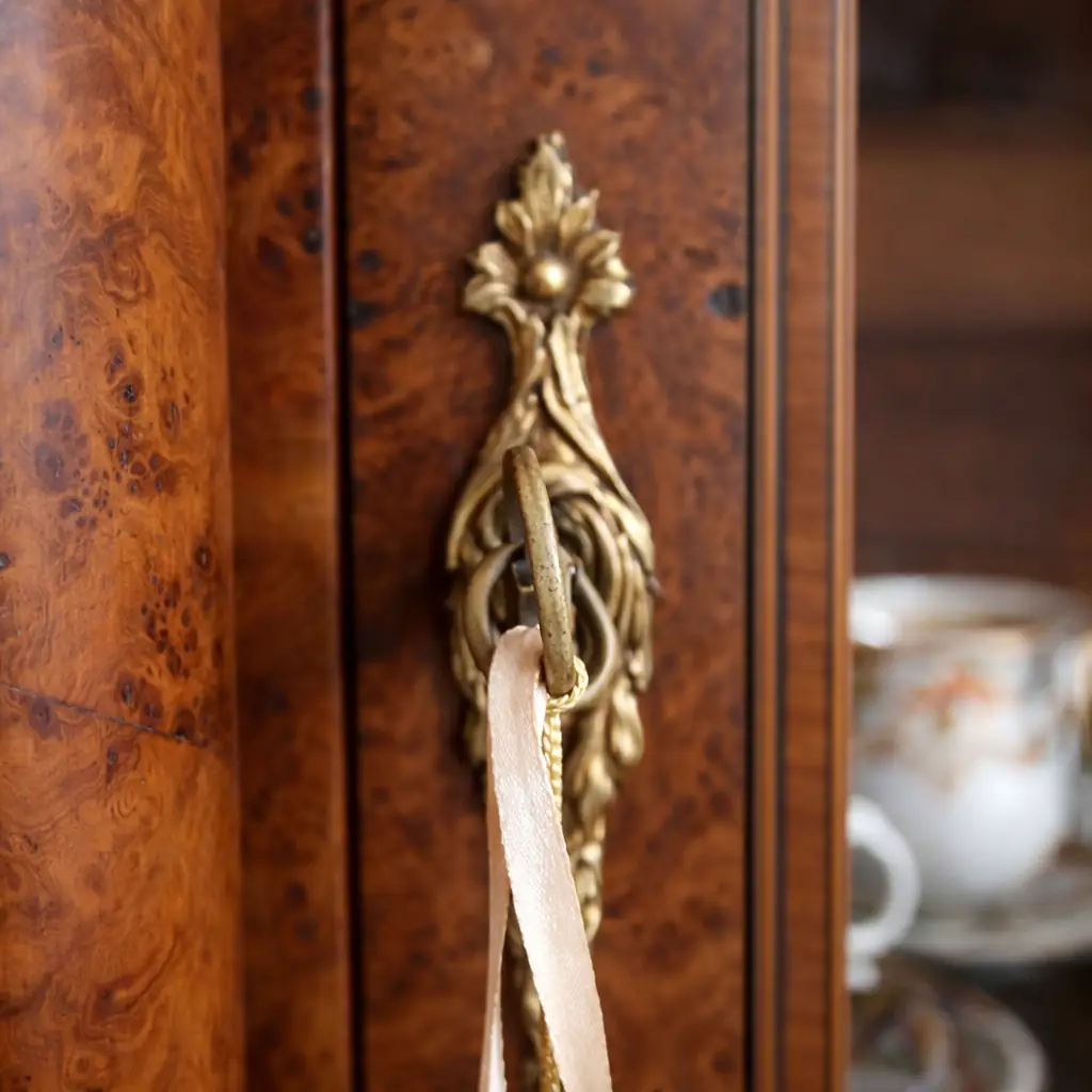 Elegante vetrina a un’anta in legno finemente impiallacciato in radica, con riserve e filettature a contrasto, riconducibile al gusto Luigi XVI / Neoclassico. Struttura architettonica con colonne laterali e anta a vetro originale, arricchita da ricche applicazioni in bronzo dorato: fregio floreale al coronamento, maniglia e guarnizioni finemente cesellate. Interni con ripiani destinati all’esposizione di porcellane. Manifattura francese o mitteleuropea, fine XIX – inizi XX secolo. Buono stato di conservazione, con patina coerente all’età e all’uso.