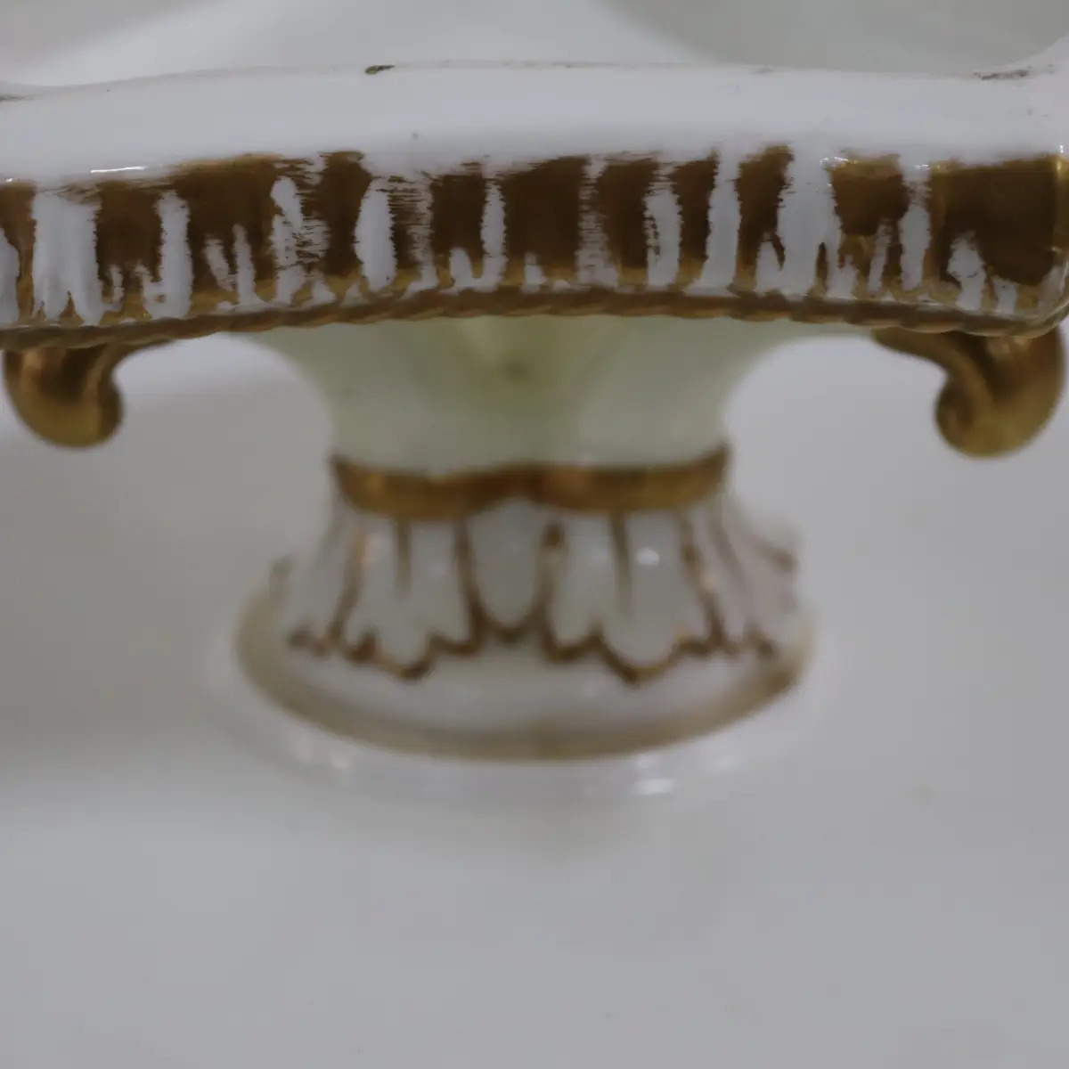 Elegante alzatina in porcellana di gusto tardo Ottocento / primi Novecento, caratterizzata da piatto sagomato con bordo ondulato e profilo dorato. La superficie è finemente decorata a motivo botanico centrale con foglie e bacche policrome, eseguite con pennellata delicata e naturalistica. Il fusto centrale poggia su una base sagomata, arricchita da elementi plastici e dorature a pennello, che conferiscono equilibrio e raffinatezza all’insieme. Oggetto da tavola o da centro, di pregiata manifattura europea, ideale come alzatina da esposizione o servizio dolci, in ottimo stato di conservazione.