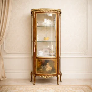 Elegante vetrina a colonna di gusto Luigi XV, realizzata in legno pregiato con struttura bombata, ricca ornamentazione in bronzo dorato e raffinati pannelli dipinti a mano con scene galanti e paesaggi di gusto settecentesco. Dotata di ante e fianchi vetrati, ripiani interni in vetro e gambe mosse con applicazioni bronzee, presenta una lavorazione accurata e armoniosa. Mobile di grande pregio decorativo, ideale per l’esposizione di porcellane, oggetti d’arte o collezioni, riconducibile alla produzione europea di fine XIX – inizi XX secolo, in ottimo stato di conservazione.