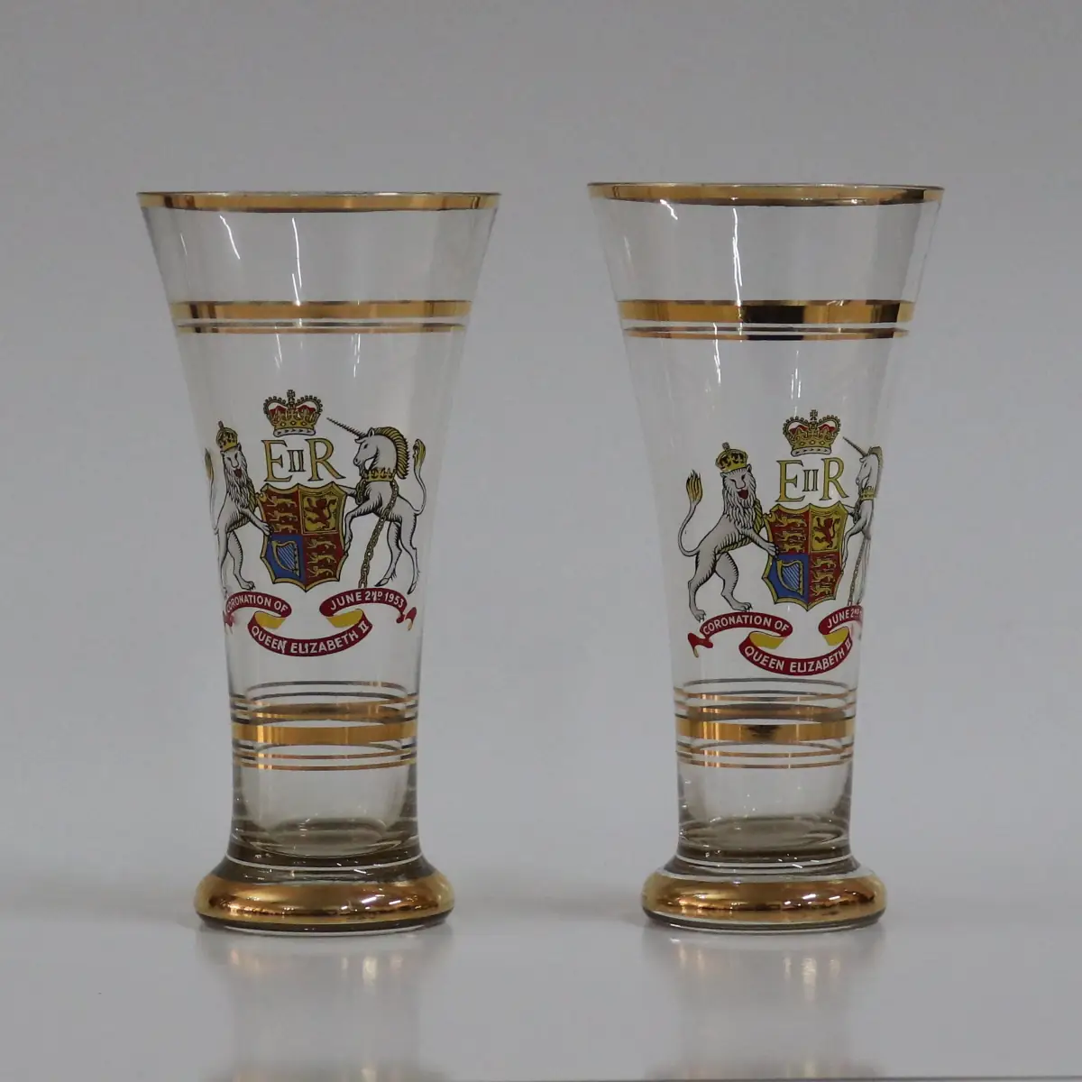 Bicchiere commemorativo in vetro trasparente, decorato con stemma reale britannico e iniziali E II R, realizzato per l’incoronazione della Regina Elisabetta II (1953). Arricchito da filettature dorate, testimonianza di produzione celebrativa d’epoca, di interesse storico e collezionistico.