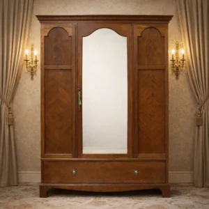 Armadio inglese di gusto Edoardiano, realizzato nei primi anni del XX secolo, in legno di mogano con elegante impiallacciatura a spina di pesce. Struttura architettonica sobria con tre ante, quella centrale a specchio, cappello modanato e cassetto inferiore con pomelli originali in ottone. Interno attrezzato con asta appendiabiti e ganci, finitura calda e ben conservata, tipica della produzione britannica di qualità.