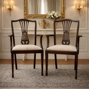 Una coppia di poltroncine di gusto sobrio ed elegante, adatte sia all’arredo d’epoca sia all’inserimento in ambienti contemporanei come elementi di contrasto di grande fascino. Coppia di poltroncine in legno massello, produzione inglese , di gusto neoclassico con richiami Luigi XVI. Schienale a giorno sagomato con stecca centrale traforata, braccioli raccordati e gambe sottili rastremate. Seduta imbottita rivestita in tessuto damascato color avorio. Finitura scura con bella patina. In ottimo stato di conservazione, strutturalmente sane e pronte all’uso.
