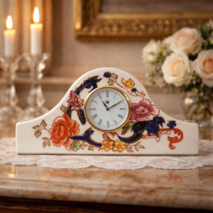 Preziosa sveglia Napoleon, orologio da camino in ceramica Mason’s Patent Ironstone, Inghilterra, decoro “Mandalay”, metà XX secolo. Cassa sagomata ad arco in smalto avorio, decorata con motivi floreali policromi di gusto orientale, volute in blu cobalto e ricche dorature. Quadrante circolare con numeri romani, cornice dorata e movimento meccanico a carica. Marchio sul retro “MASON’S – Mandalay – ENGLAND”. In molto buone condizioni generali. Oggetto decorativo e da collezione.