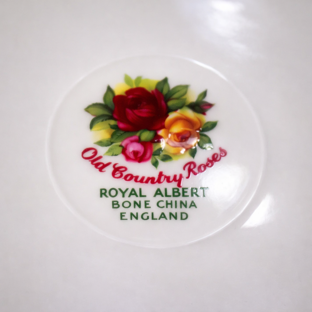Tazza da tè con piattino “Old Country Roses” – Royal Albert, Inghilterra Elegante tazza da tè con doppio piattino in fine porcellana Bone China, produzione inglese Royal Albert, celebre decoro Old Country Roses. La tazza, dal profilo leggermente svasato con ansa sagomata, poggia su piede ad anello; il piattino presenta bordo mosso con marcata ondulazione e ricca filettatura in oro. La decorazione raffigura mazzetti di rose nei toni del rosso, rosa e giallo con fogliame verde, disposti sul corpo della tazza e lungo la tesa del piattino; interno con fascia dorata al bordo. Ottimo stato di conservazione. Classico esempio della produzione Royal Albert della seconda metà del Novecento, molto apprezzato per la qualità della porcellana e la vivacità del decoro.