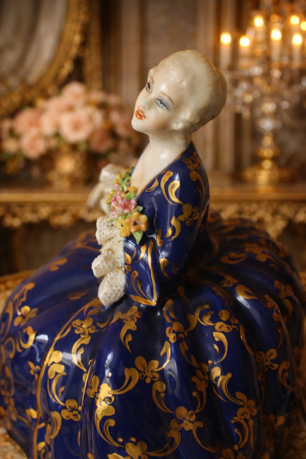 Raffinata statuina in porcellana policroma di manifattura Fabris, raffigurante elegante dama in abiti settecenteschi seduta, con ricco abito blu cobalto impreziosito da dorature a foglia e motivi ornamentali di gusto rococò. Il busto è finemente modellato, con volto delicato, incarnato luminoso e bouquet floreale applicato sul petto; presenti dettagli a rilievo e accurata smaltatura. La base sagomata completa la composizione con armonia ed equilibrio. Manifattura: Fabris Epoca: XX secolo Stato di conservazione: ottimo.