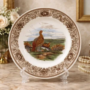 Piatto in ceramica ironstone inglese, manifattura Mason’s, serie Game Birds – Common Partridge (Perdix cinerea), con scena centrale policroma raffigurante coppia di pernici in paesaggio naturale. Ampia tesa decorata da ricca bordura a girali, riserve figurate e motivi ornamentali in tonalità seppia, con profilo sagomato. Marchio sul retro “Mason’s Patent Ironstone – Made in England”. Produzione della prima metà del XX secolo. In buono stato di conservazione.