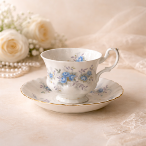 Tazza da tè con piattino “Blue Blossom” – Royal Albert, 1988 Elegante tazza da tè con piattino in fine porcellana Bone China inglese, produzione Royal Albert, decoro Blue Blossom, come da marchio sul fondo datato 1988. La tazza, dal profilo leggermente bombato con ansa sagomata, poggia su piccolo piede ad anello; il piattino presenta tesa delicatamente ondulata con sottile filettatura in oro al bordo. La decorazione è composta da roselline azzurre con fogliame verde e tocchi lilla, disposte a ghirlanda sul piattino e in motivo continuo sulla tazza; piccolo fiore interno. Ottimo stato di conservazione, senza sbeccature o restauri evidenti, con lievi segni d’uso compatibili con l’età. Grazioso esempio della produzione inglese tardo-novecentesca, adatto a collezione o a un’elegante tavola in stile classico.