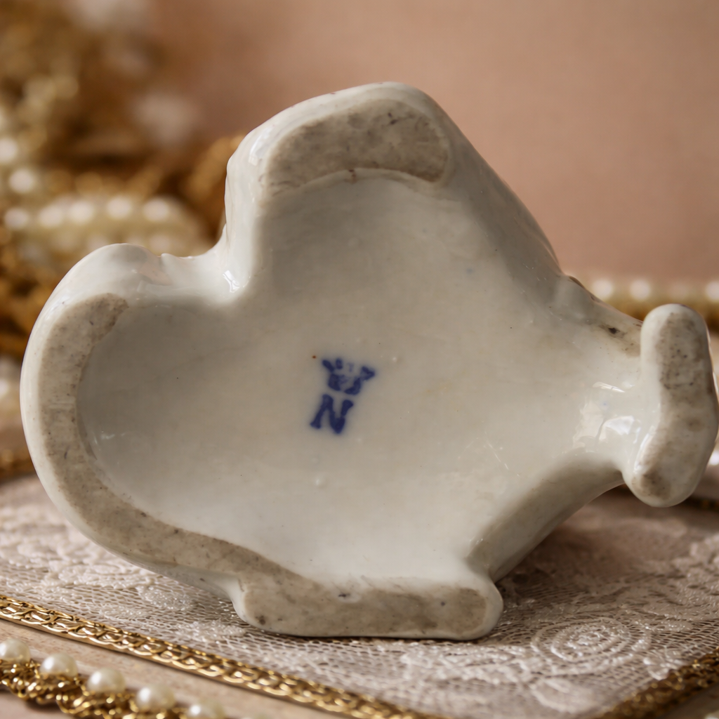 Importante statuina in porcellana di Capodimonte, raffigurante figura femminile allegorica seduta su base mossa a volute rocaille. La dama, vestita con ricchi panneggi policromi e dorature a rilievo, è rappresentata nell’atto di scrivere su un libro aperto, simbolo delle Arti o delle Lettere. Finissima la modellazione anatomica, accurata la decorazione floreale e preziosa la smaltatura. Sul fondo è presente marchio N coronata dipinta in blu. Manifattura: Capodimonte Epoca: 19° secolo ( produzione di gusto settecentesco) Stato di conservazione: buono.