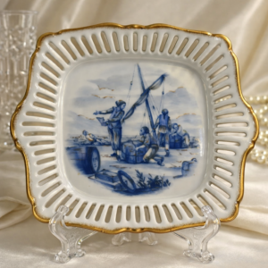 Piatto in porcellana traforata dipinta in blu cobalto, Atelier Porcelaine d’Art, XX secolo.Forma quadrilobata con tesa traforata e bordi dorati; al centro scena marina con pescatori, ispirata alla tradizione figurativa settecentesca di Dresda e Meissen, resa in monocromia blu. Retro con iscrizioni storicizzanti e marchio di atelier. Buono stato di conservazione. Oggetto decorativo di gusto neoclassico, da collezione.