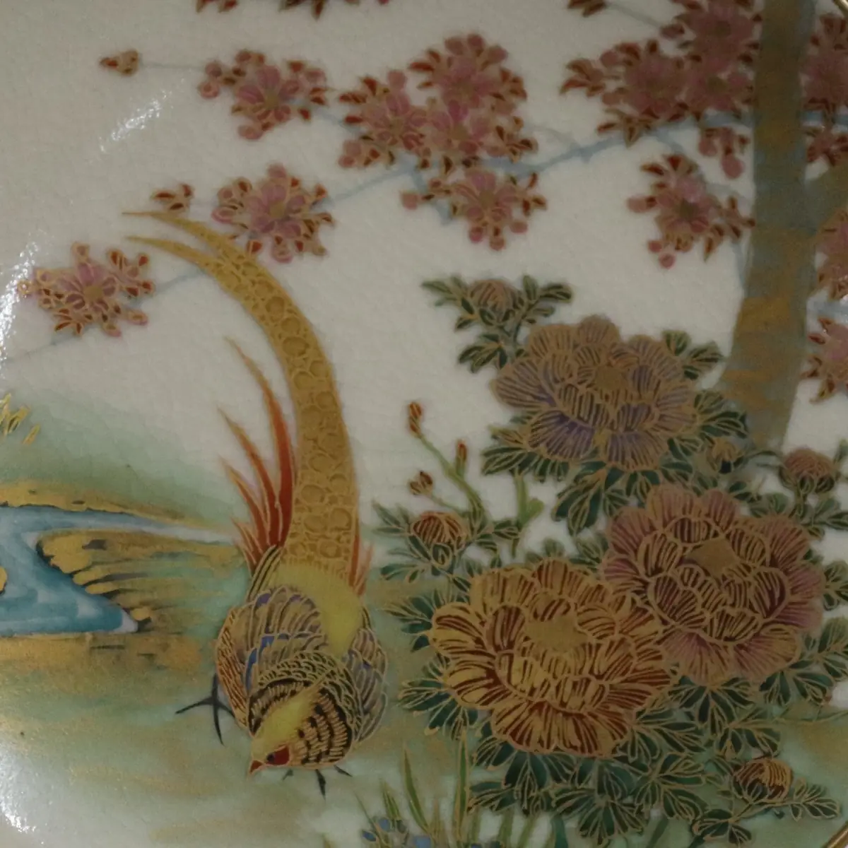 Piatto Satsuma giapponese in ceramica finemente decorata, Giappone, periodo Meiji (fine XIX – inizi XX secolo). Il cavetto presenta una raffinata scena naturalistica con fagiano tra crisantemi e rami fioriti, resa con minuziosa policromia e ricchi dettagli in oro. Bordo sagomato e dorato. Al verso marchio Satsuma con iscrizione Hand Painted, indicativo di produzione destinata al mercato occidentale. Esemplare decorativo di qualità, rappresentativo della tradizione pittorica Satsuma.