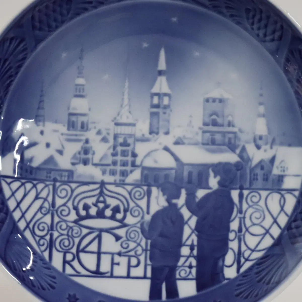 Piatto da collezione in porcellana Royal Copenhagen, Danimarca, decorato in blu cobalto sotto smalto. La scena raffigura una veduta urbana innevata con bambini affacciati a una balaustra ornamentale, sullo sfondo di torri e tetti storici sotto il cielo stellato. Appartenente alla rinomata serie dei piatti natalizi, è apprezzato per l’eleganza compositiva, il gusto architettonico e l’elevata qualità pittorica.