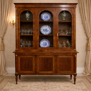 Elegante credenza/vetrina in legno massello, Italia prima metà XIX secolo, di gusto Impero–Restaurazione. Corpo a due corpi: alzata con ante vetrate ad arco per l’esposizione e base con ante pannellate scanalate. Linee sobrie ed equilibrate, montanti a colonnina, piedi torniti. Patina calda e finiture originali; mobile funzionale e di grande presenza decorativa.