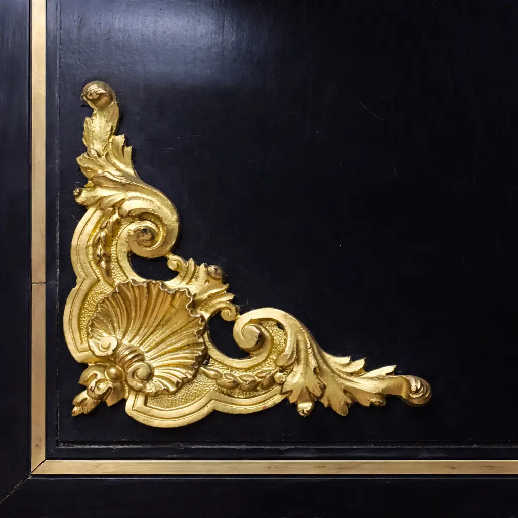 Vetrina alla Boulle in ebano, tartaruga e bronzi dorati Francia, seconda metà del XIX secolo – Stile Napoleone III Raffinata vetrina a un’anta realizzata secondo la celebre tecnica “alla Boulle”, con impiallacciatura in ebano e ricchi intarsi in ottone su fondo in tartaruga rossa naturale, disposti in eleganti motivi a racemi e volute di gusto Luigi XIV. Il prospetto è impreziosito da importanti applicazioni in bronzo dorato finemente cesellato, raffiguranti figure allegoriche laterali, fregi a foglie d’acanto e mascherone centrale nella parte inferiore. L’anta vetrata, incorniciata da profili dorati, apre su ripiani interni destinati all’esposizione di porcellane e oggetti d’arte. Esempio di alta ebanisteria francese del periodo Napoleone III, il mobile coniuga ricchezza ornamentale, equilibrio architettonico e forte impatto scenografico, risultando ideale per ambienti di rappresentanza o collezioni antiquarie di pregio.