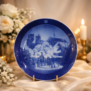 Piatto da parete in porcellana a pasta dura della manifattura danese Royal Copenhagen, appartenente alla serie natalizia annuale “Jul på Slottet / Christmas at the Manor House”, anno 1997. Decorazione sottosmalto in blu cobalto con scena invernale raffigurante gruppo familiare intento alla scelta dell’albero di Natale, con architetture ecclesiastiche innevate sullo sfondo; tesa ampia decorata a rilievo con stella e data modellata. Marchio verde al verso con corona, tre onde e dicitura Denmark. Produzione del XX secolo, ottimo stato di conservazione, oggetto da collezione.