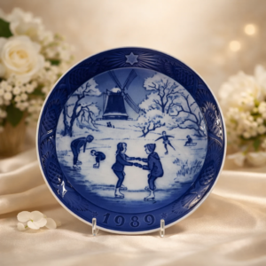 Piatto da parete in porcellana a pasta dura della manifattura danese Royal Copenhagen, appartenente alla serie natalizia annuale “Jul på Slottet / Christmas at the Manor House”, anno 1989. Decorazione sottosmalto in blu cobalto con scena invernale raffigurante bambini che pattinano su lago ghiacciato, con mulino e paesaggio innevato sullo sfondo; tesa decorata a rilievo con stella e data modellata. Marchio verde al verso con corona, tre onde e dicitura Denmark. Produzione del XX secolo, in ottimo stato di conservazione, oggetto da collezione.