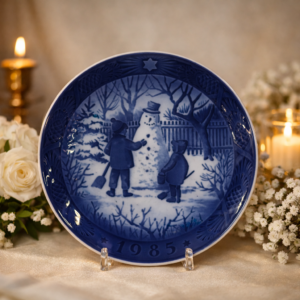 Piatto decorativo in porcellana danese Royal Copenhagen, serie natalizia “Jul på Slottet / Christmas at the Manor House”, datato 1985. Decorazione blu cobalto sottosmalto con scena invernale raffigurante due bambini intenti a costruire un pupazzo di neve. Marchio verde al verso con corona e dicitura Royal Copenhagen Denmark. Produzione del XX secolo, ottimo stato di conservazione, oggetto da collezione.