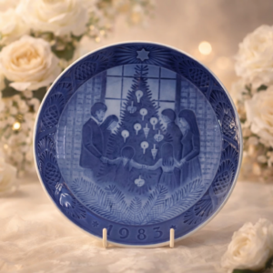 Piatto commemorativo natalizio in porcellana – Royal Copenhagen, 1983 Piatto da collezione in porcellana smaltata a decorazione monocroma blu sottocobalto, appartenente alla serie natalizia annuale della manifattura Royal Copenhagen. Datato 1983 in rilievo sul fronte. La decorazione centrale raffigura una scena d’interno con famiglia riunita attorno all’albero di Natale, resa con eleganti gradazioni di blu e composizione di carattere tradizionale. Bordo decorato a rilievo con motivi vegetali e stella simbolica. Al verso, marchio originale Royal Copenhagen con corona reale, tre onde e dicitura Copenhagen – Denmark, con titolo bilingue “Jul på Slottet / Christmas at the Manor House”. Stato di conservazione: ottimo. Oggetto da collezione.