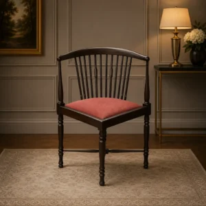Elegante poltroncina inglese ad angolo di gusto vittoriano, realizzata in legno massello con raffinato schienale curvo a colonnine tornite disposto a ventaglio. La particolare struttura avvolgente richiama i celebri modelli Corner Chair inglesi, apprezzati per comfort ed eleganza negli ambienti signorili tra Otto e Novecento. La seduta imbottita, rivestita in tessuto rosso damascato, crea un piacevole contrasto con la calda tonalità del legno. Le gambe tornite unite da traverse incrociate sagomate conferiscono stabilità e armonia alla struttura.