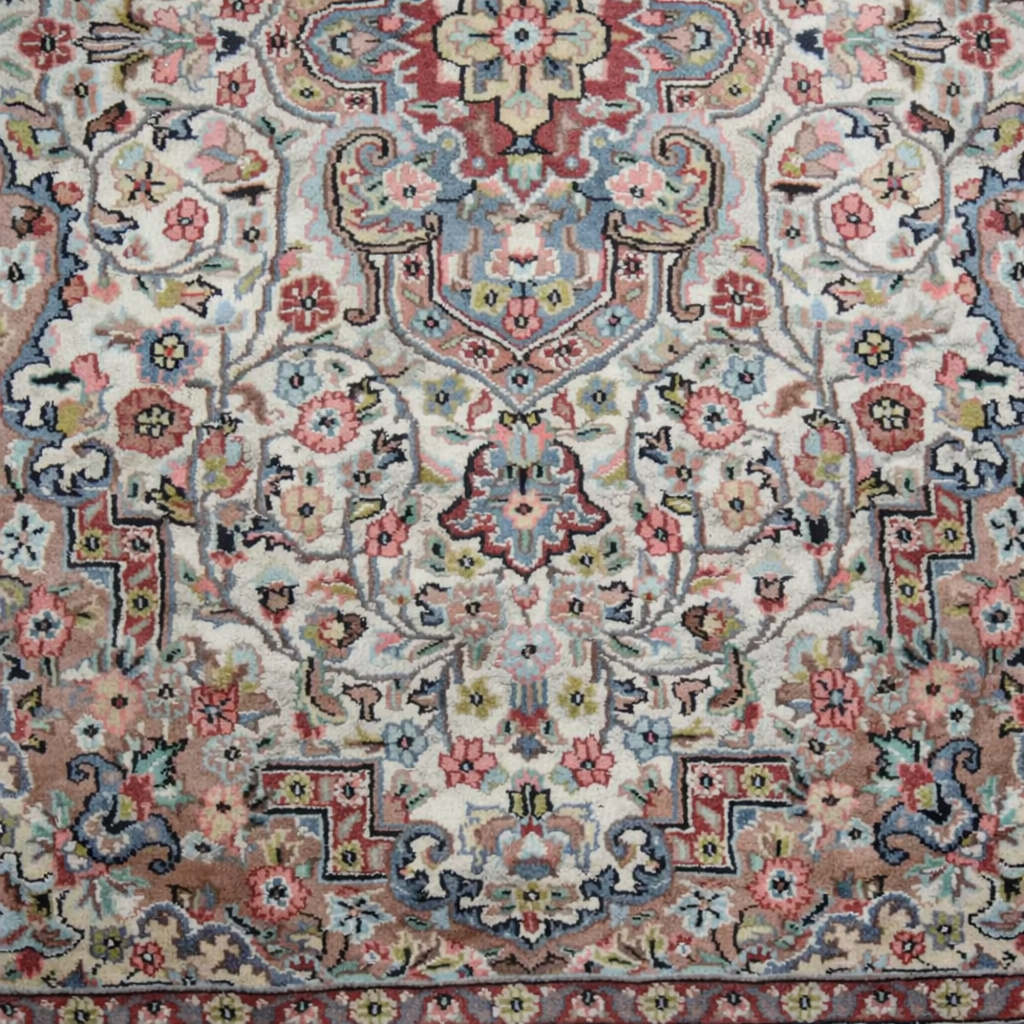 Elegante tappeto orientale di manifattura persiana, annodato a mano in lana su ordito in cotone, caratterizzato da un armonioso medaglione centrale su campo avorio riccamente decorato da motivi floreali e vegetali stilizzati. La composizione è racchiusa da una raffinata bordura a fondo azzurro-grigio con decori policromi coordinati. La palette cromatica, nei toni dell’avorio, rosa, azzurro, celeste e rosso mattone, dona luminosità e delicatezza all’insieme. Il tappeto si presenta in ottimo stato di conservazione, con vello compatto e colori ben conservati. Ideale per valorizzare salotti, studi o ambienti classici. Dimensioni: cm 190 x 130
