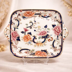 Vassoio con manici – Mason’s “Mandalay” Inghilterra, prima metà del XIX secolo Elegante vassoio da portata in porcellana inglese con manici laterali sagomati, produzione Mason’s Patent Ironstone, decoro “Mandalay”. La forma quadrangolare con angoli arrotondati è impreziosita da una ricca bordura blu cobalto profilata in oro, che incornicia un raffinato motivo floreale policromo di gusto orientale, con peonie e tralci stilizzati. Decorazione stampata e rifinita a mano; marchio al verso “Mason’s – Patent Ironstone – Mandalay – Made in England”, riferibile alla produzione della seconda metà del Novecento. In eccellente stato di conservazione, senza difetti evidenti. Oggetto di grande eleganza, ideale per una tavola importante o per arricchire una collezione di porcellane inglesi.