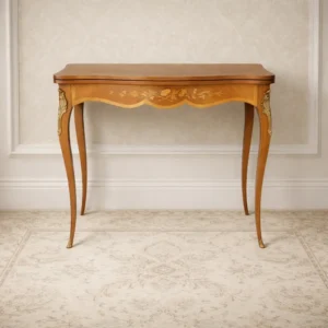 Tavolino da gioco / scrittoio in stile Luigi XV – fine XIX secolo Raffinato tavolino francese di fine Ottocento, realizzato in legno con pregiate impiallacciature e delicati intarsi floreali in essenze chiare. Il piano sagomato è impreziosito da una composizione centrale a bouquet e da motivi vegetali agli angoli, con elegante disposizione delle venature. Dotato di piano apribile che rivela un interno rivestito in panno verde e vano contenitore, il mobile si presta sia all’uso come tavolino da gioco sia come scrittoio. La fascia mossa è decorata da intarsio floreale, mentre le gambe slanciate presentano applicazioni in bronzo dorato nella parte superiore. Mobile di grande eleganza e qualità decorativa, espressione del gusto Luigi XV revival. Condizioni: molto buone, con lievi segni del tempo coerenti con l’età.